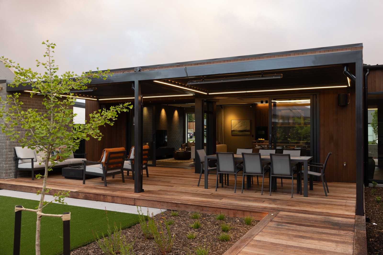 Outdoor dining terrace under a steel louvred pergola at dusk, Hallmark Homes Oakbridge showhome