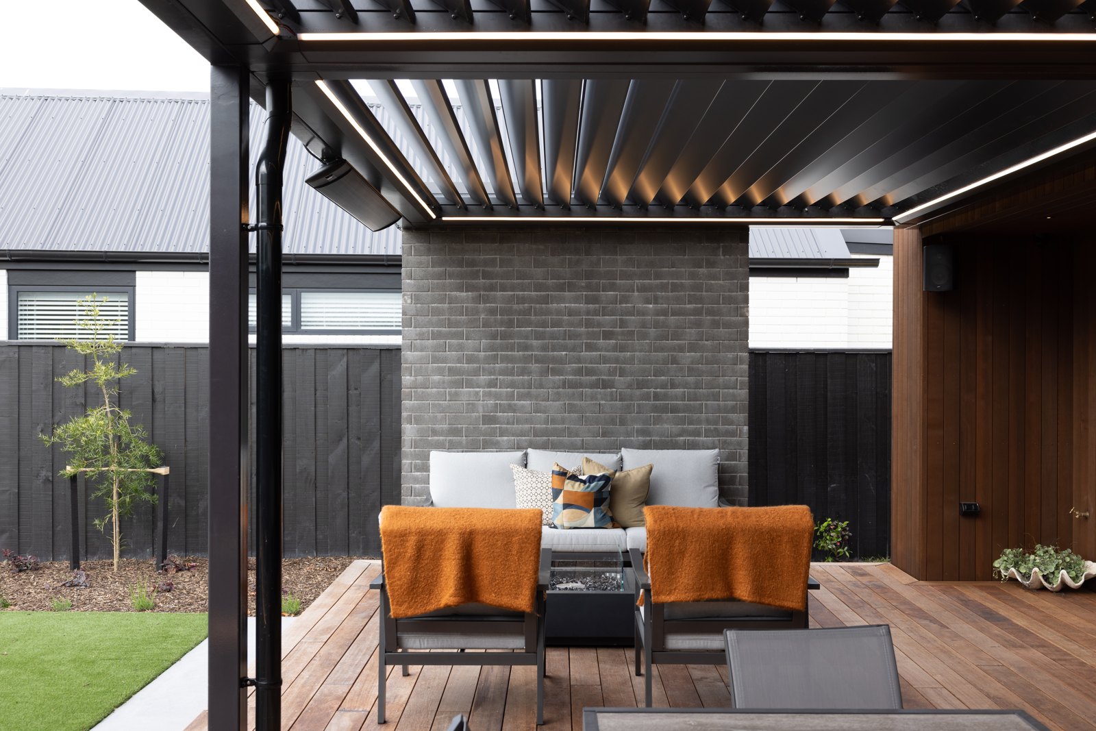 Sheltered outdoor lounge under a steel pergola against a brick wall, Hallmark Homes Oakbridge
