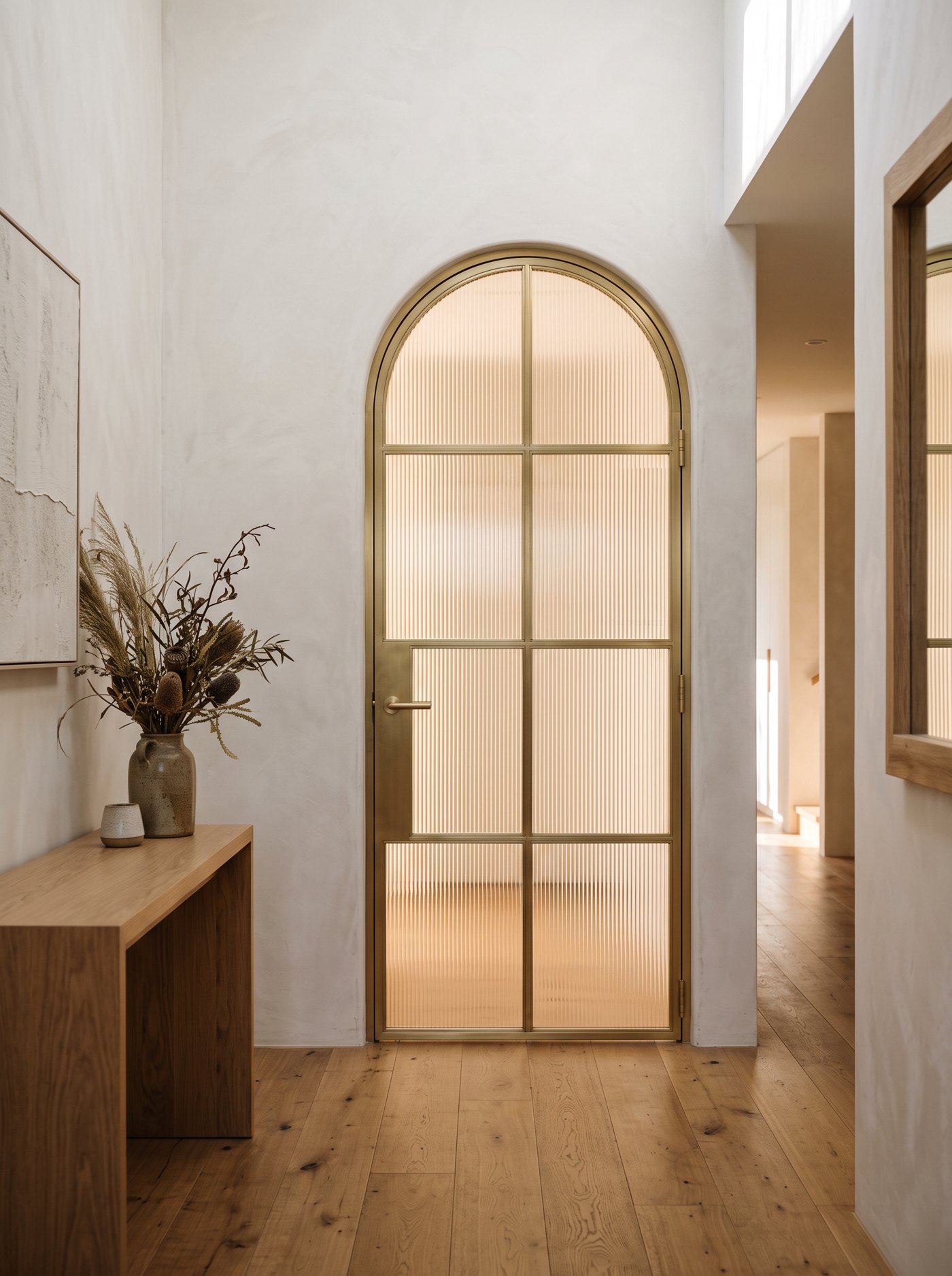 Arched brushed-brass steel door with reeded fluted glass in a hallway