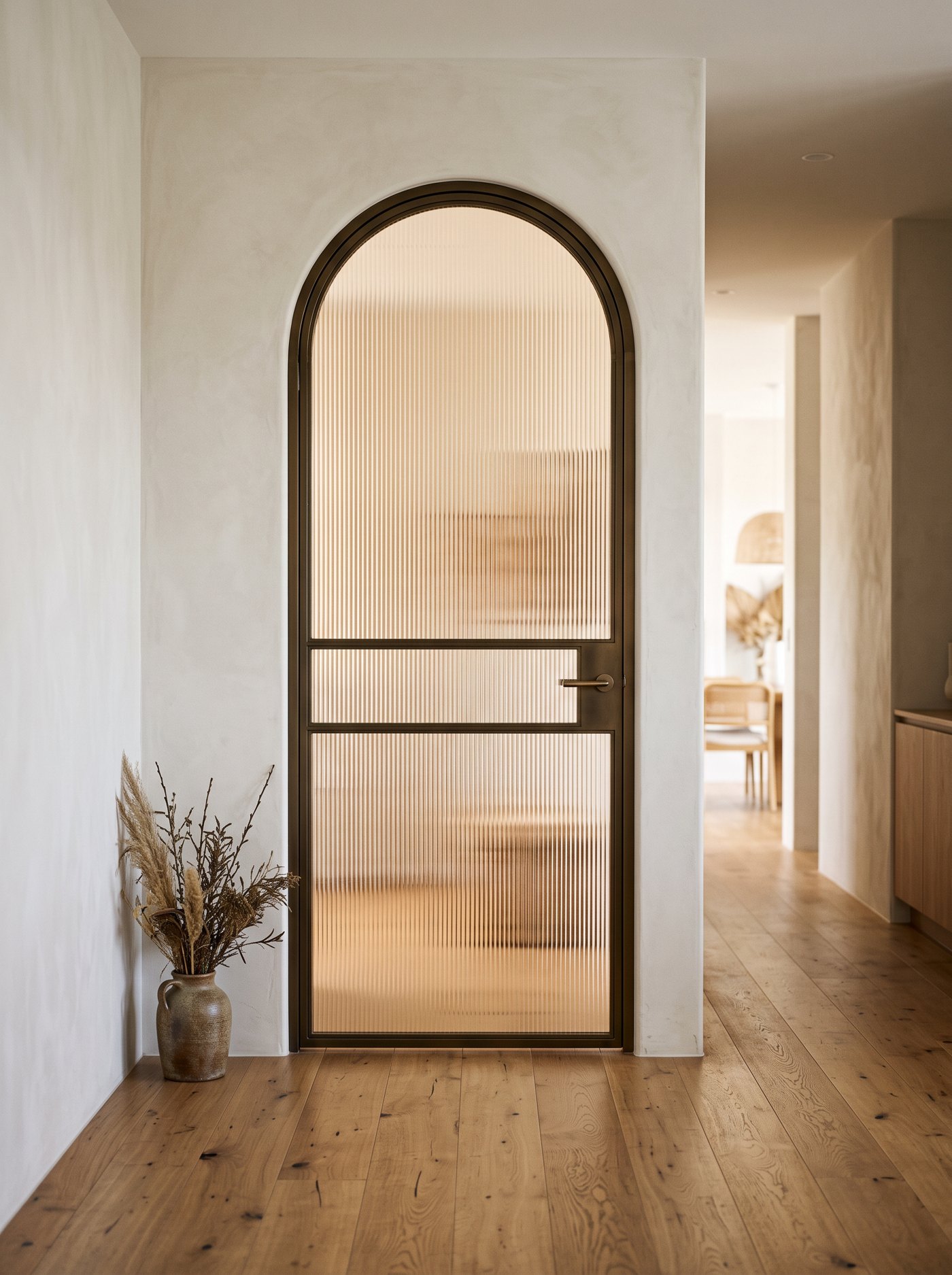Arched bronze steel door with reeded fluted glass and a horizontal rail