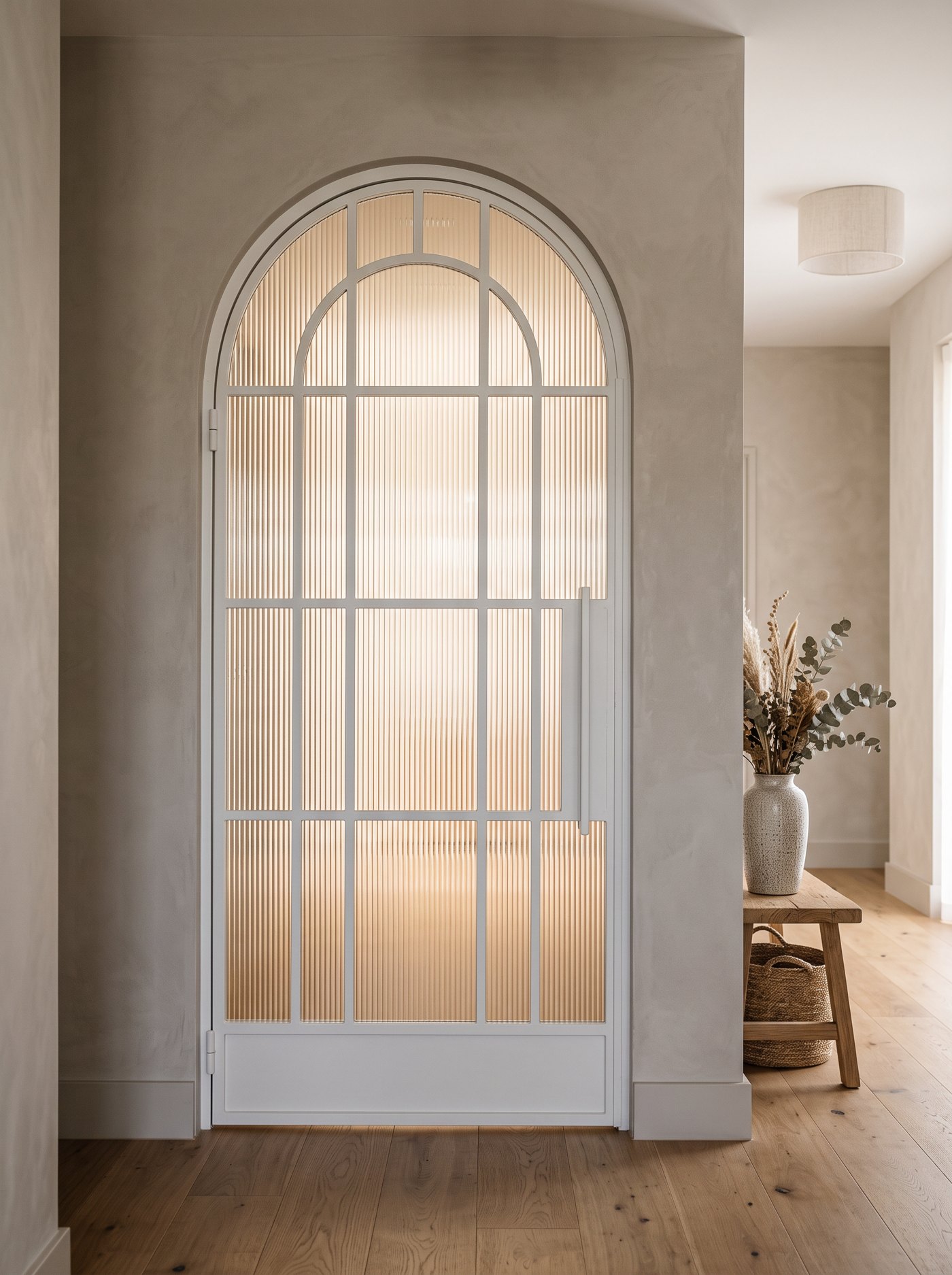 White arched steel door with a concentric arch head and reeded fluted glass in a warm plaster hallway